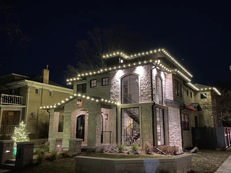 Stone and stucco home with warm white C9 lights tracing every roofline and gable